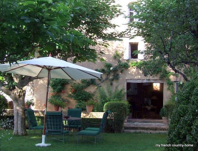 garden with large umbrella, chairs, and a house visible through the trees