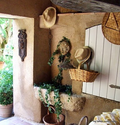 summertime-living-easy-2-my-french-country-home stone room with baskets and hats on a wall