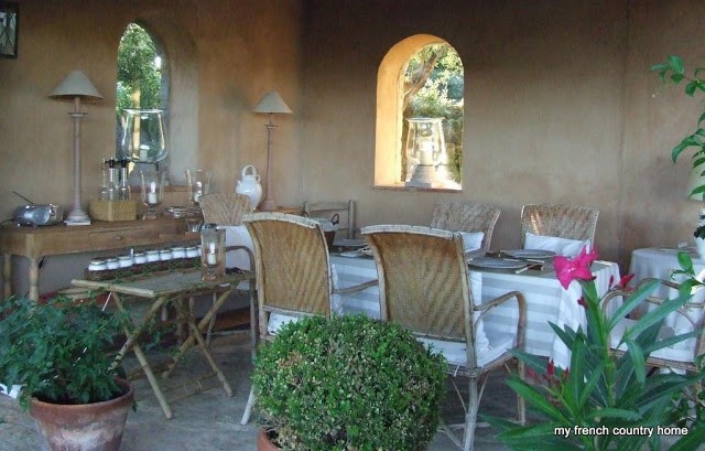 summertime-living-easy-2-my-french-country-home semi-enclosed outdoor dining space with striped tablecloth and wicker chairs