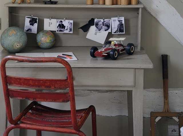 neutral beige desk with photos, small globes, and a red metal chair