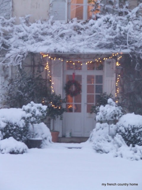 front door with lights and a wreath, with snow covered wisteria above