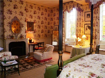 bedroom with floral-patterned wallpaper, four-poster bed and a fireplace with sitting area