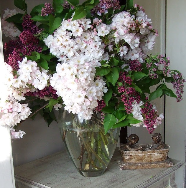 glass vase with lilac blossoms and ornamental cherry branches
