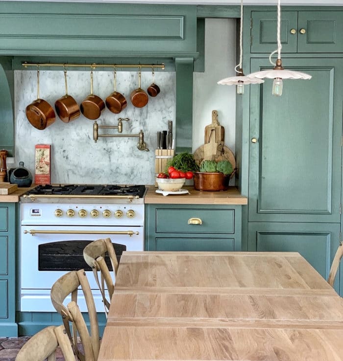 french kitchen with long wooden table, green walls and copper pots and pans