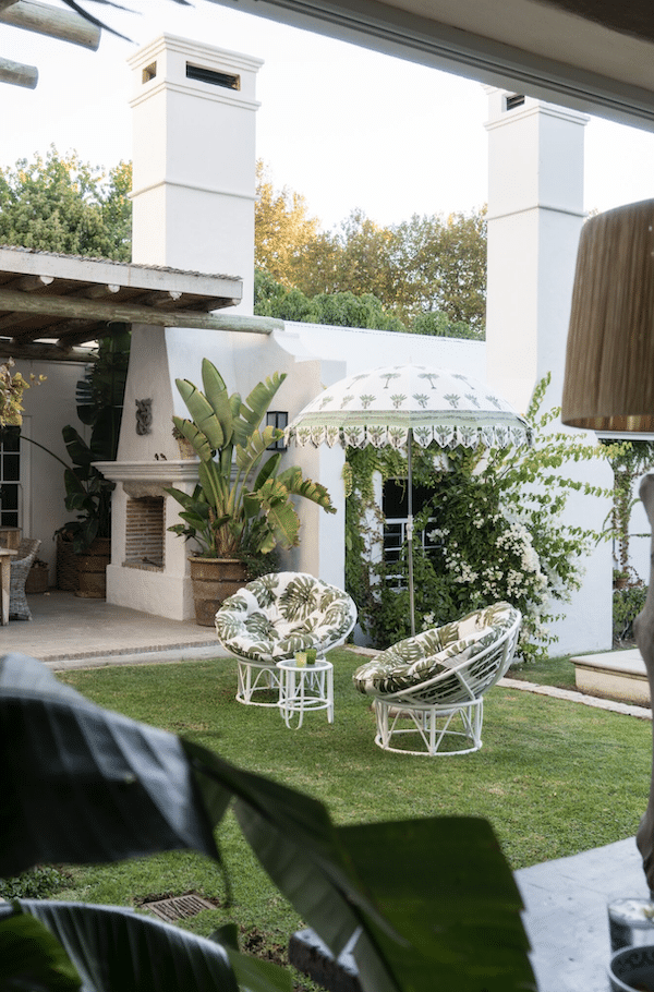 two outdoor chairs with cushions on lawn in front of white house with plants