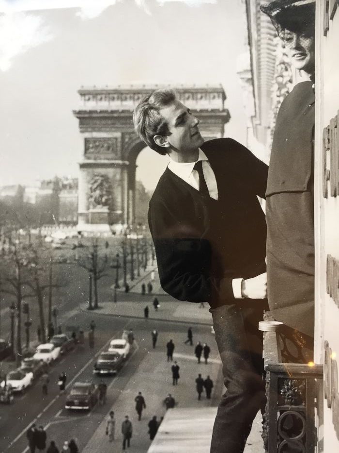 man and woman leaning outside window in front of arc de triumph