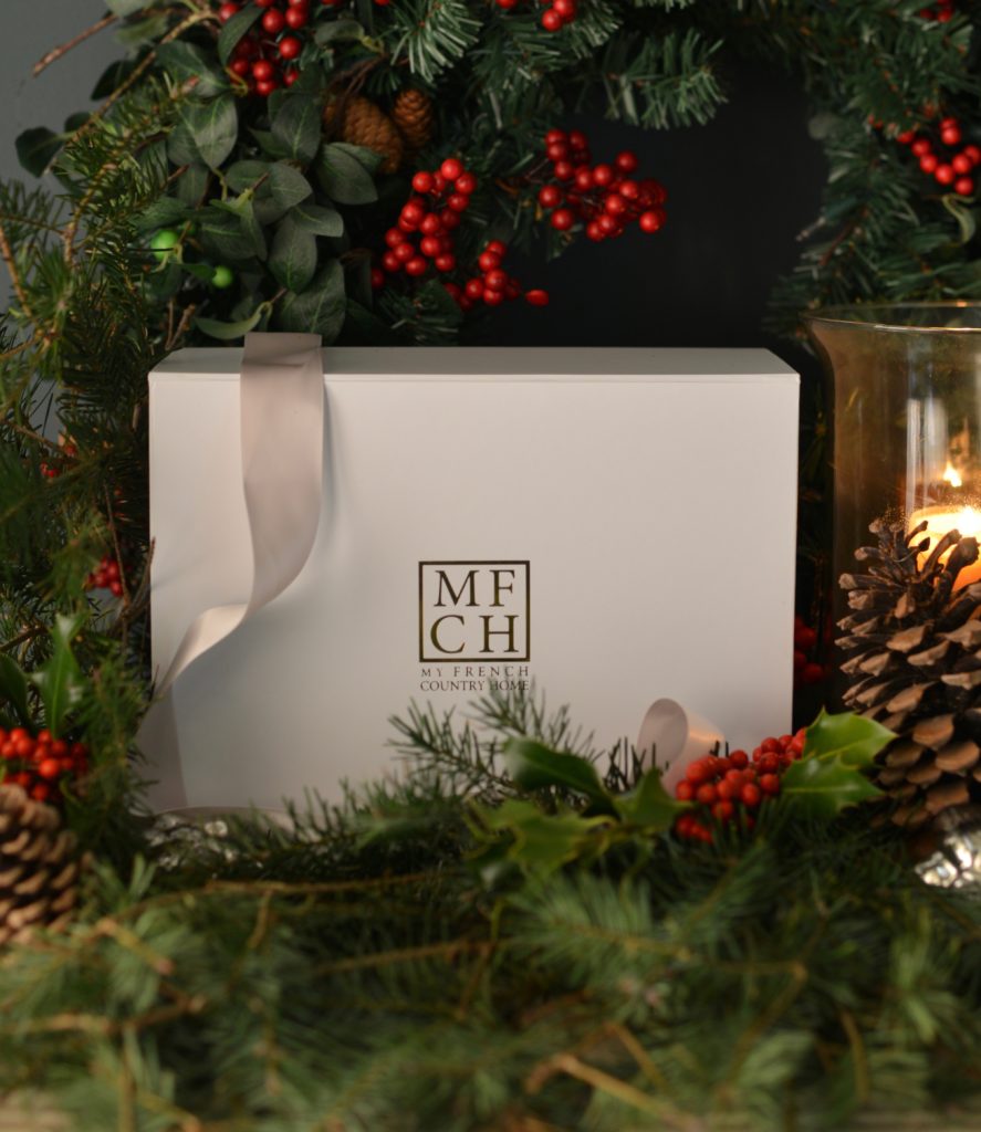 white subscription box with ribbon, holly, pine cones and pine branches